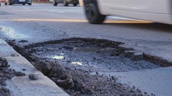 Buca nell'asfalto e strada con auto